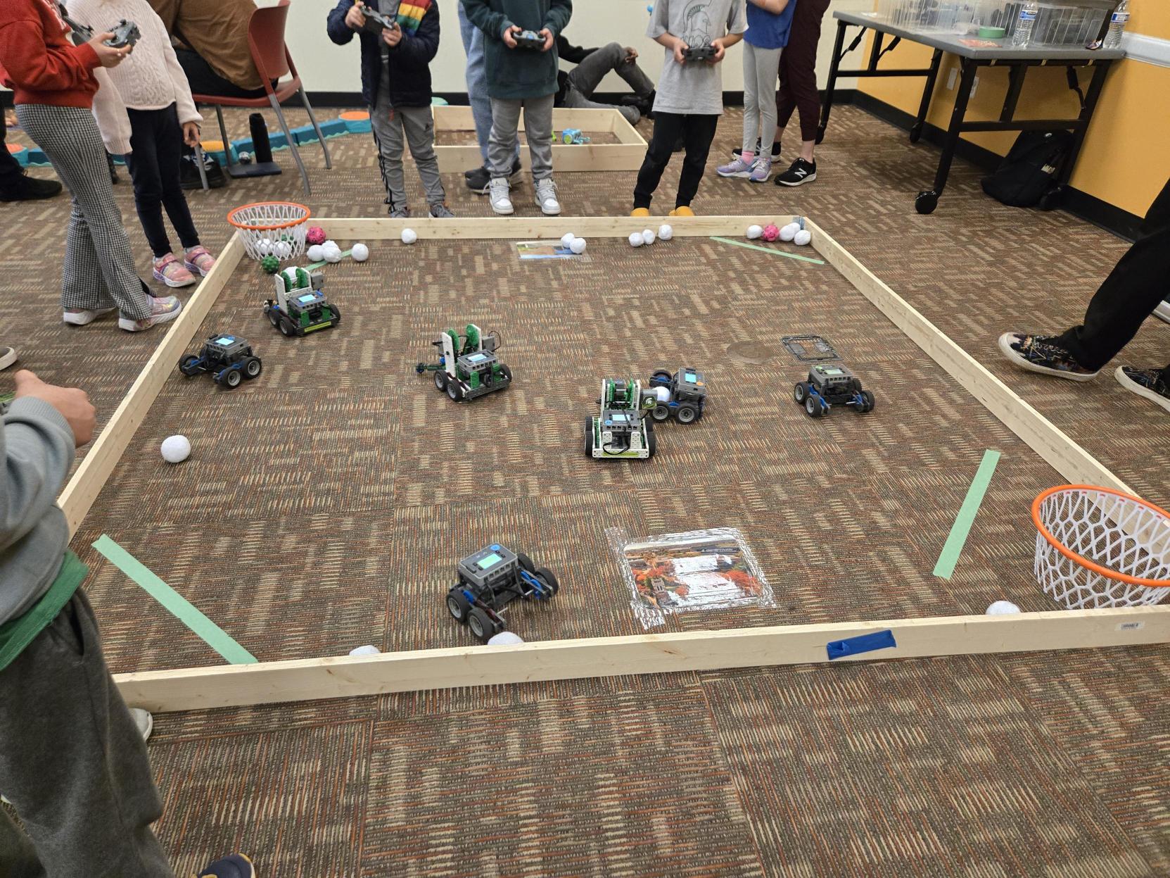 Youth standing around a square with their robots inside.